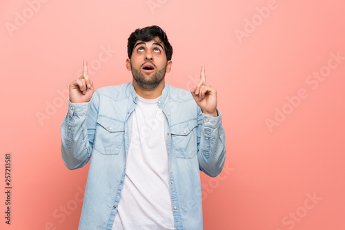 Young man over pink wall surprised and pointing up
