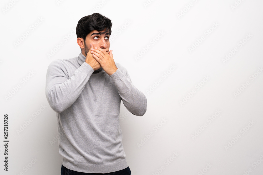 Young man over isolated white wall covering mouth and looking to the side Young man over isolated white wall covering mouth and looking to the side