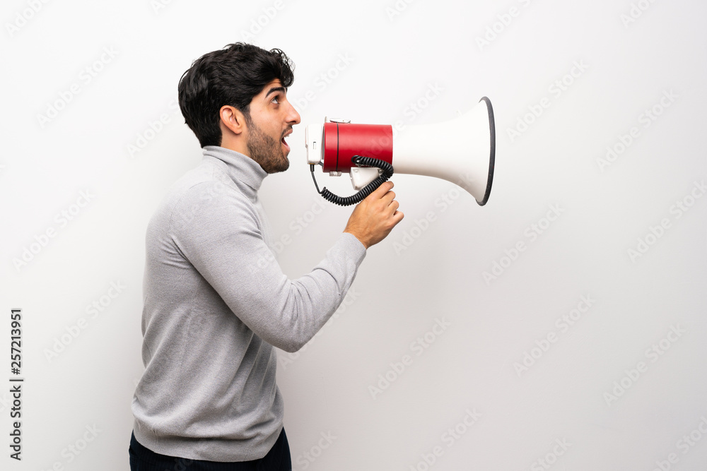 Young man over isolated white wall shouting through a megaphone Young man over isolated white wall shouting through a megaphone