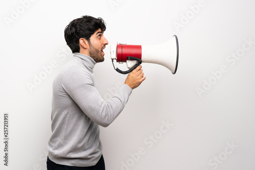 Young man over isolated white wall shouting through a megaphone