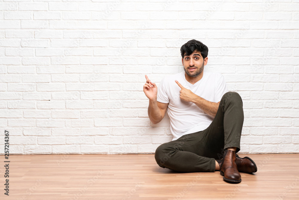 Young man sitting on the floor frightened and pointing to the side Young man sitting on the floor frightened and pointing to the side