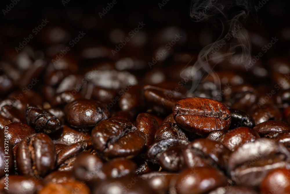 Dark brown roasted coffee beans with smoke under artificial light for background