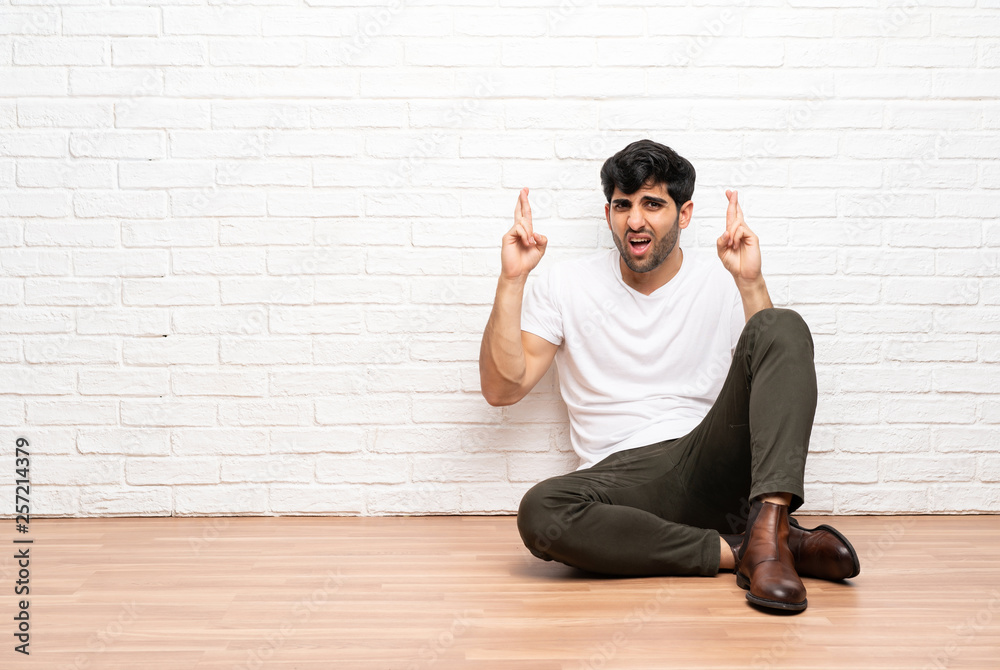 Young man sitting on the floor with fingers crossing Young man sitting on the floor with fingers crossing