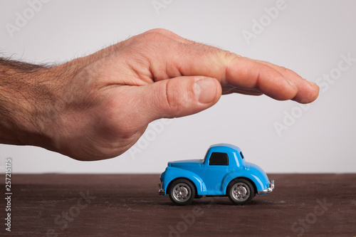 Small retro, blue car covering by male hand. Protection, car insurance.