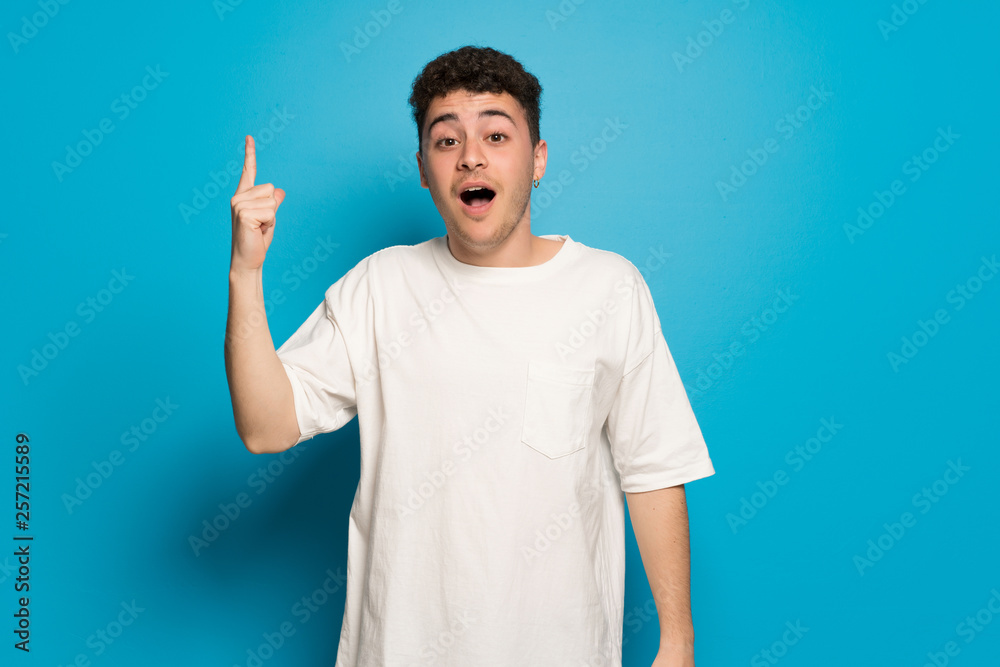Young man over blue background intending to realizes the solution while lifting a finger up