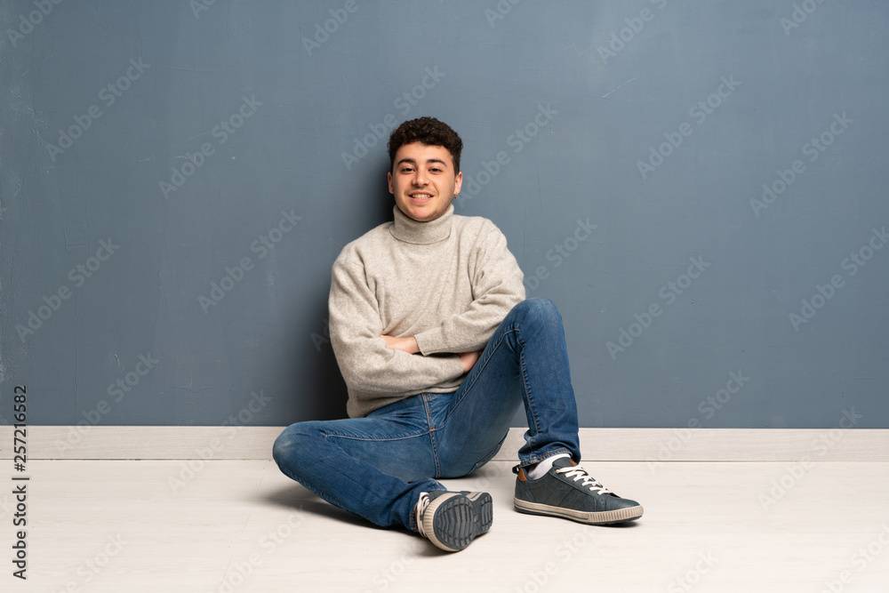 Young man sitting on the floor keeping the arms crossed in frontal position Young man sitting on the floor keeping the arms crossed in frontal position