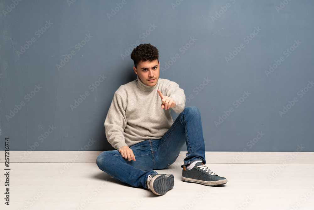 Young man sitting on the floor frustrated and pointing to the front Young man sitting on the floor frustrated and pointing to the front