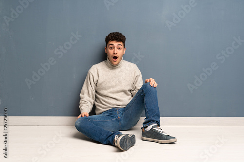 Young man sitting on the floor with surprise facial expression