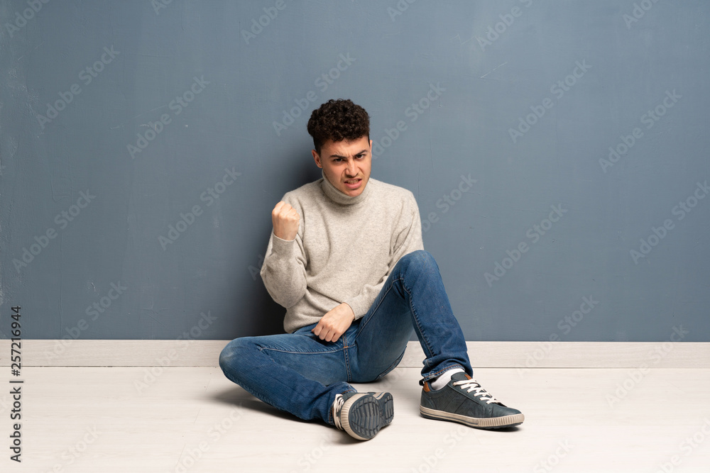 Young man sitting on the floor with angry gesture