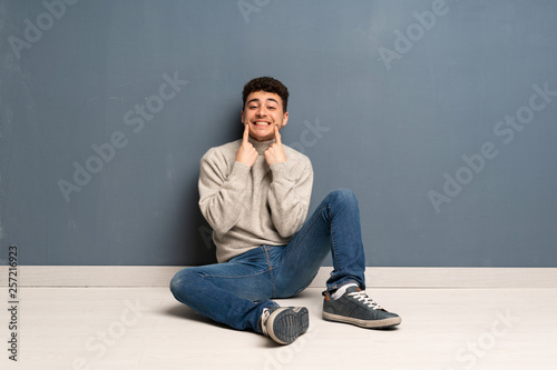 Young man sitting on the floor smiling with a happy and pleasant expression
