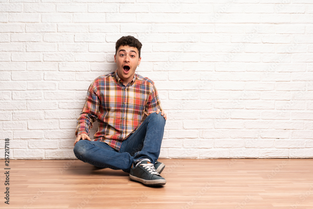 Young man sitting on the floor with surprise facial expression