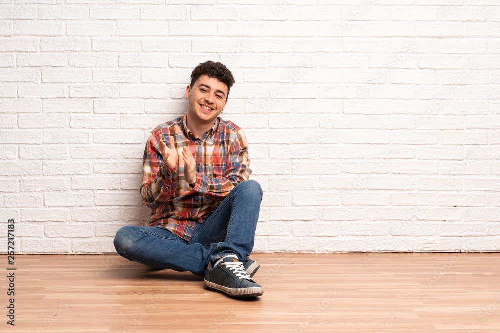 Young man sitting on the floor applauding after presentation in a conference Young man sitting on the floor applauding after presentation in a conference