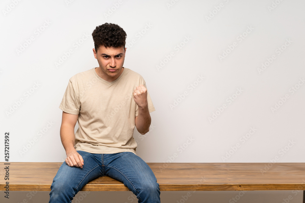 Young man sitting on table with angry gesture Young man sitting on table with angry gesture