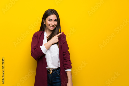 Young woman over yellow wall pointing to the side to present a product