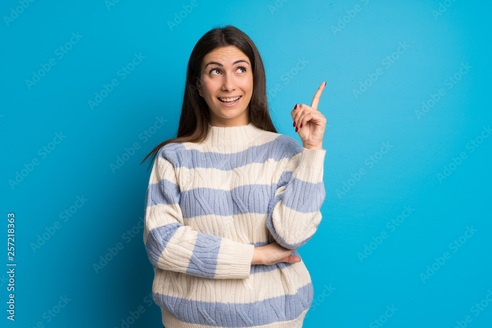 Young woman over blue wall pointing a great idea and looking up Young woman over blue wall pointing a great idea and looking up