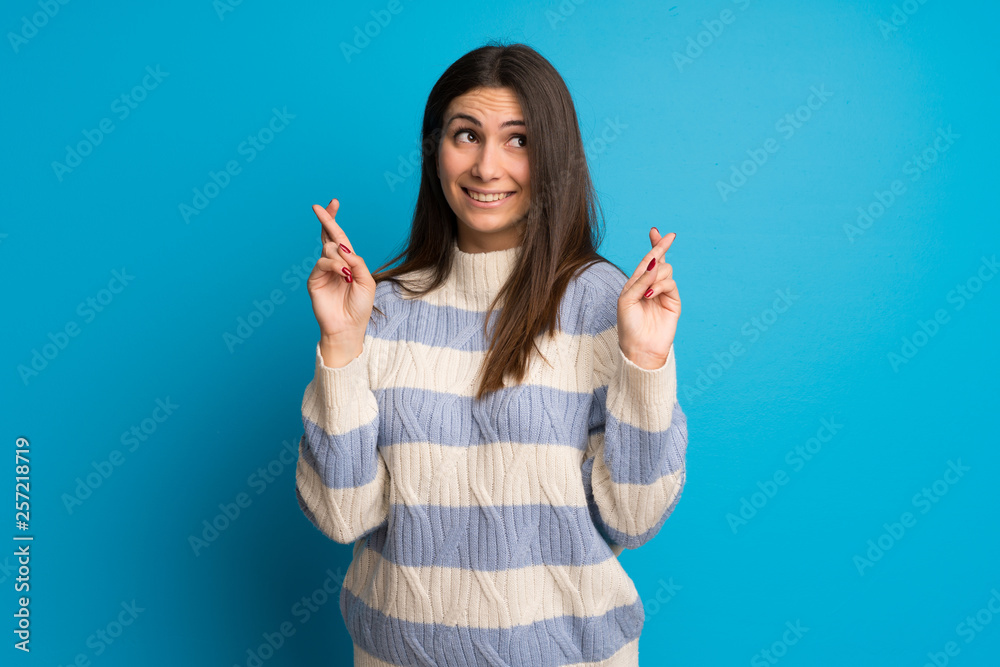 Young woman over blue wall with fingers crossing and wishing the best Young woman over blue wall with fingers crossing and wishing the best