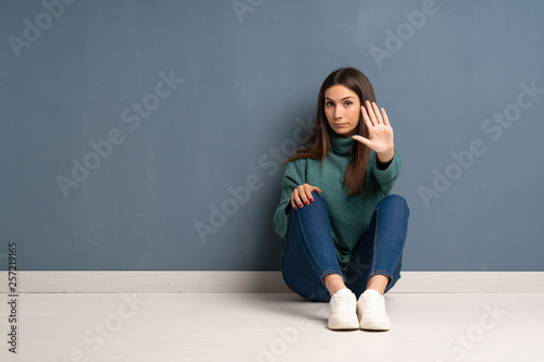 Young woman sitting on the floor making stop gesture denying a situation that thinks wrong