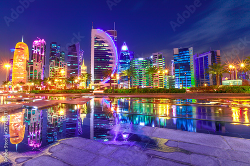 Capital of Qatar. Colorful Doha West Bay high rises illuminated at night reflections in downtown park. Scenic towers of Doha skyline, Middle East, Arabian Peninsula in Persian Gulf. Violet colors shot photo