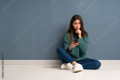 Young woman sitting on the floor thinking and sending a message