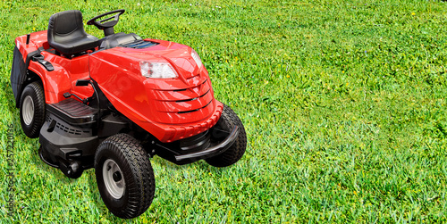 Gardening equipment advertisement template - red tractor mower on a green grass in the garden with copy space.