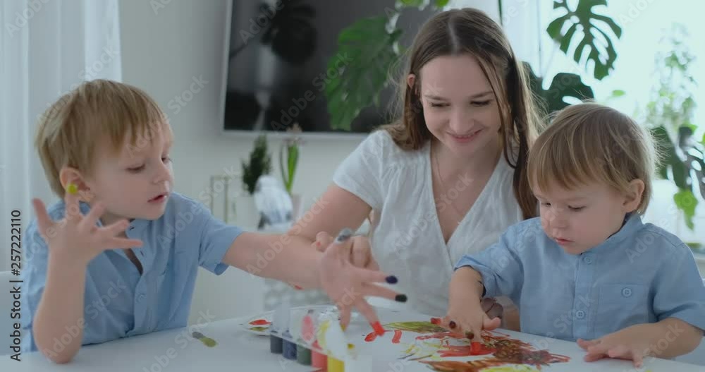 The family has fun painting on paper with their fingers in paint. Mom and two children paint with fingers on paper The family has fun painting on paper with their fingers in paint. Mom and two children paint with fingers on paper