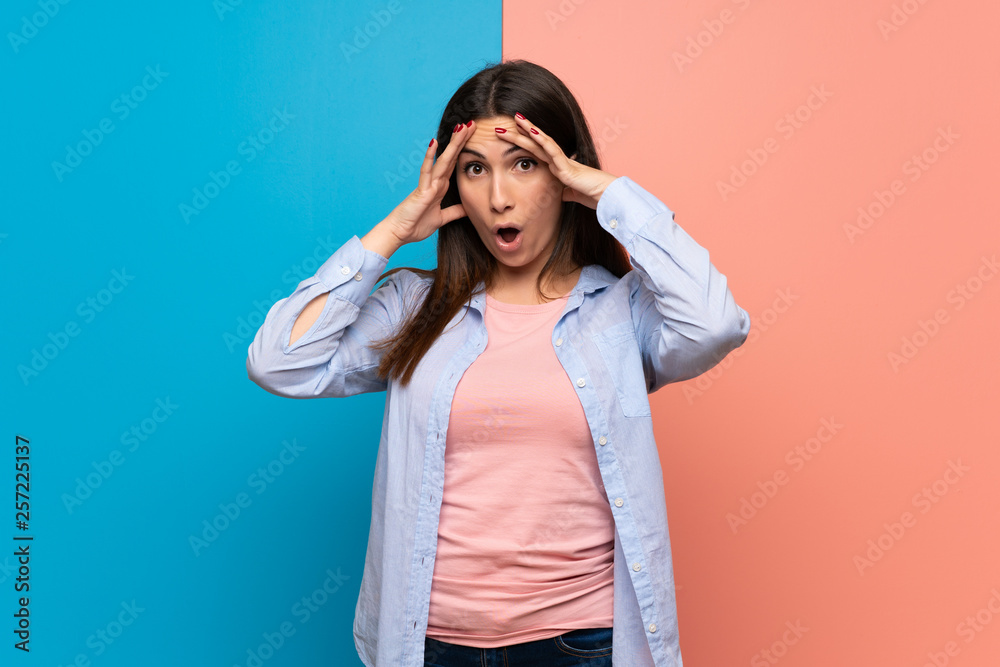 Young woman over pink and blue wall with surprise and shocked facial expression Young woman over pink and blue wall with surprise and shocked facial expression