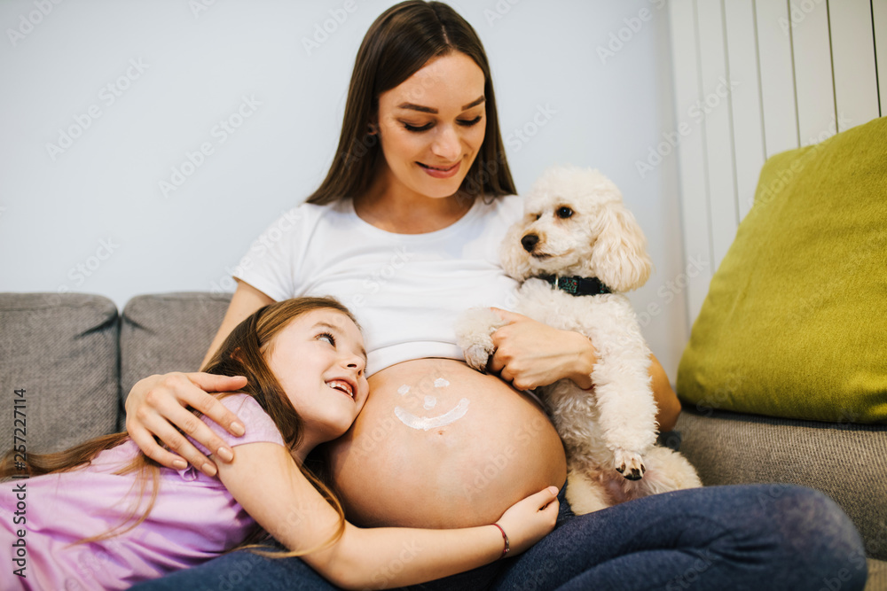 Young pregnant woman enjoying with her cute daughter and poodle. Young pregnant woman enjoying with her cute daughter and poodle.