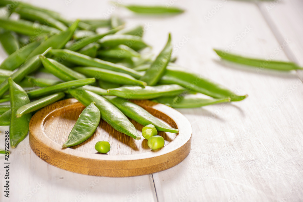 Lot of whole green sugar snap pea on bamboo plate on white wood Lot of whole green sugar snap pea on bamboo plate on white wood