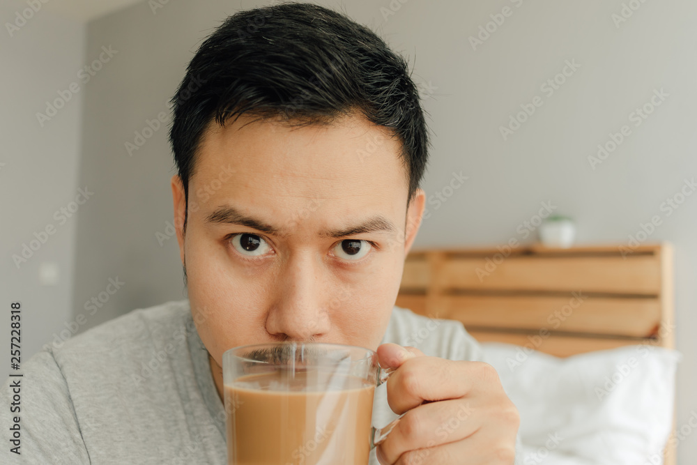 Man is drinking a cup of coffee on the bed in his bedroom. Man is drinking a cup of coffee on the bed in his bedroom.