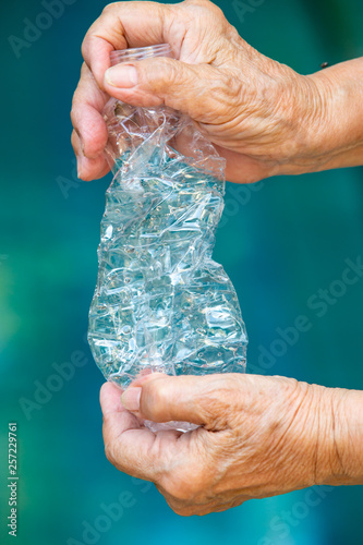 Senior woman's hand squashing used plastic bottle, Recycle concept, Blue swimming pool background