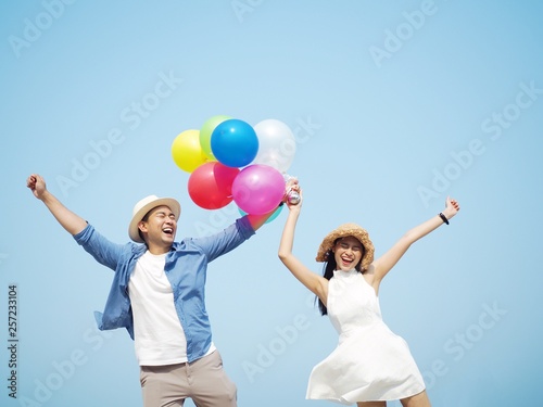 Happy Asian couple lover holding balloons standing over blue sky background.  © Mallika