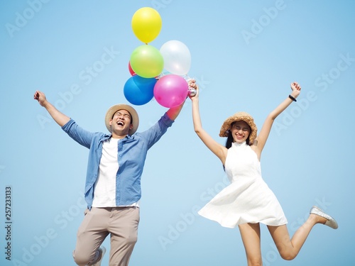 Happy Asian couple lover holding balloons standing over blue sky background.  © Mallika