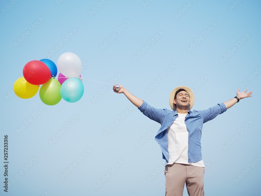 Happy Asian man holding colorful of balloons over blue sky background. Happy Asian man holding colorful of balloons over blue sky background.