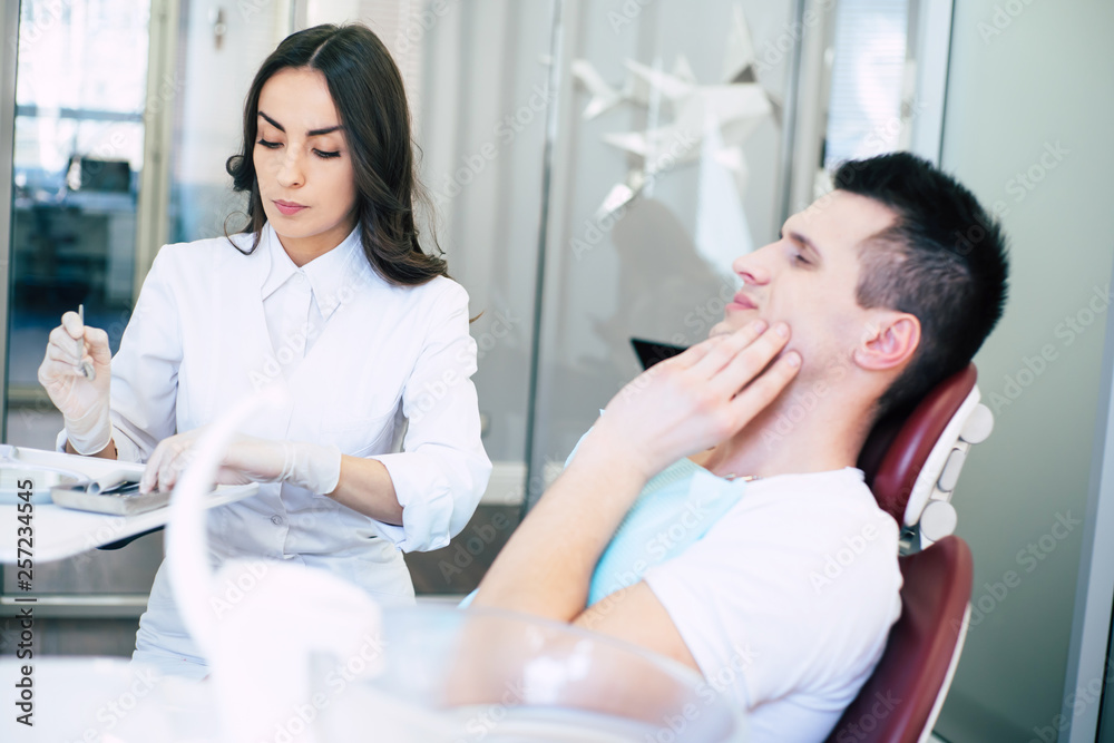 Obraz premium Periodontics. Professional doctor of dental clinic is in process of giving treatment to the patient who is having a hard pain in his teeth and it can be seen in his gestures.