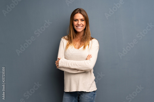 Blonde woman over grey background with arms crossed and looking forward