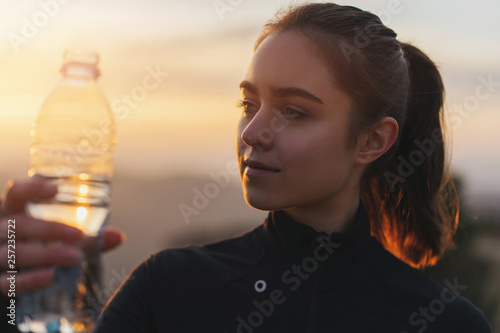 Portrait of young sporty girl drinking water after running at the sunset , Drinking water concept