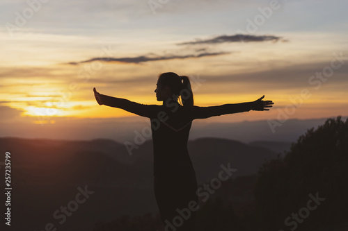 Silhouette of athletic girl with arms outstretched from the mountain in the background at sunset
