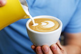 Closeup cup of cappuccino. Barista holding and pouring milk to make latte art