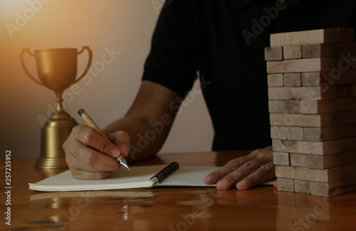 woman bussiness hand writeing on note book with block wooden game on wooden table