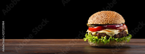 Homemade hamburger close-up with beef, tomato, lettuce, cheese and onion on wooden table. Fastfood on dark background