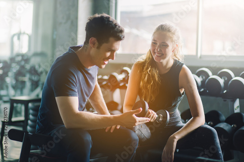 young man and personal trainer with dumbbell muscles in gym, sport, fitness, teamwork, weightlifting and people concept. Fitness girl lifting dumbbell in the morning. Change for health concept.