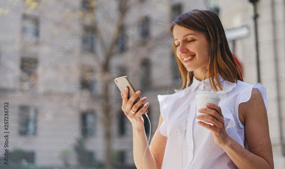 Lifestyle portrait of happy woman walking in the city on a sunny summer day while making video call via smart phone