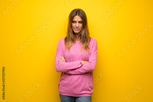 Woman with pink sweater over yellow wall looking to the side