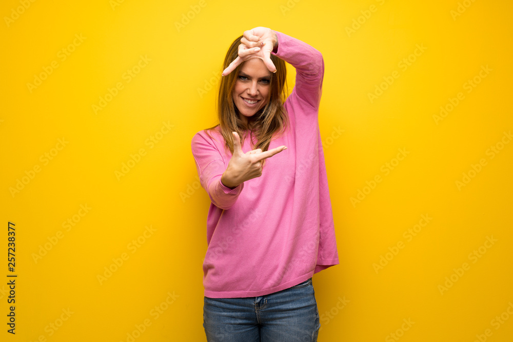 Woman with pink sweater over yellow wall focusing face. Framing symbol Woman with pink sweater over yellow wall focusing face. Framing symbol