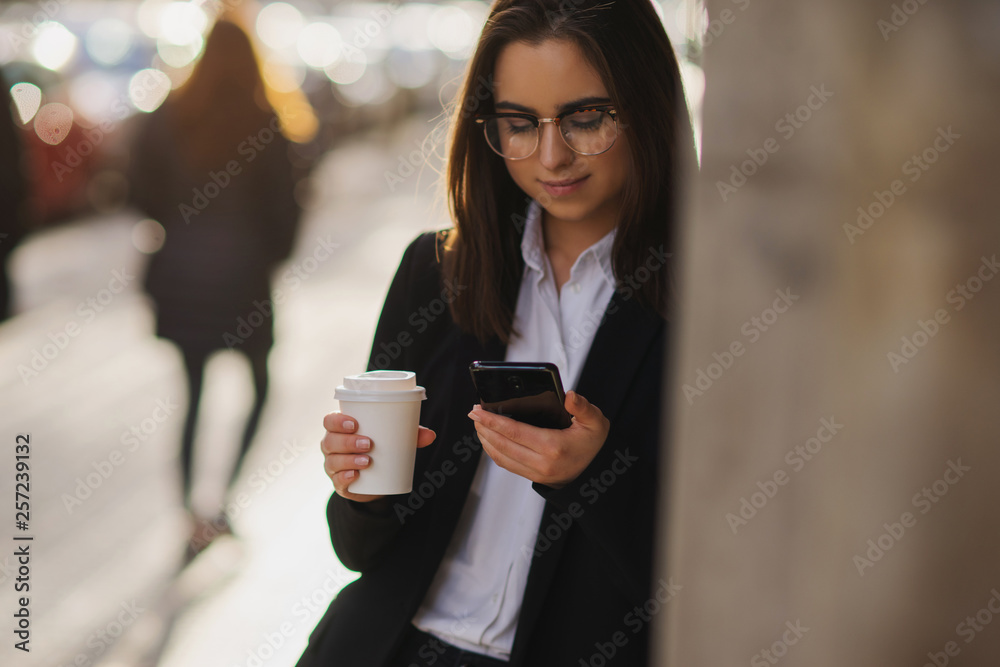 Smiling female student talking via mobile phone and drinking coffee on the city street Smiling female student talking via mobile phone and drinking coffee on the city street