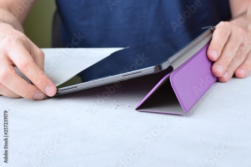 White man‘s hands holding a new tablet and put on a purple leather case with selective focus. Man using a tablet. Putting on a violet protection cases for personal tablet. Tablet accessories