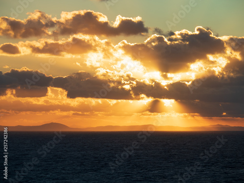 Sun rays burst out from behind clouds as the sunset over the ocean