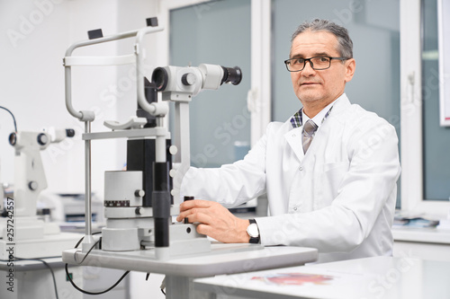 Doctor ophthalmologist posing with slit lamp in cabinet.