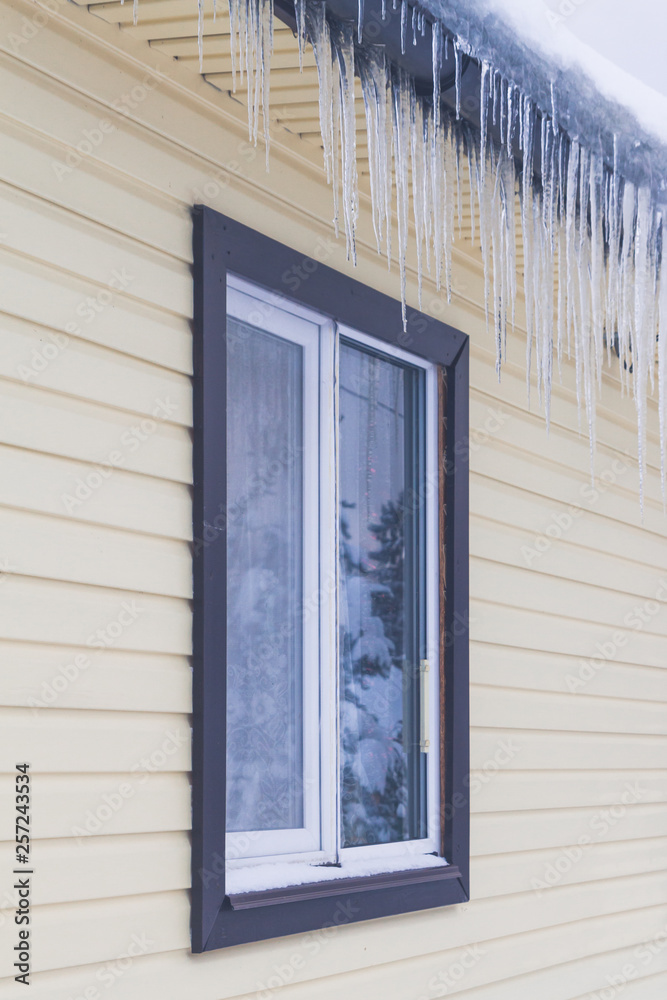 Fototapeta premium Icicles hang from the roof of a private house in winter