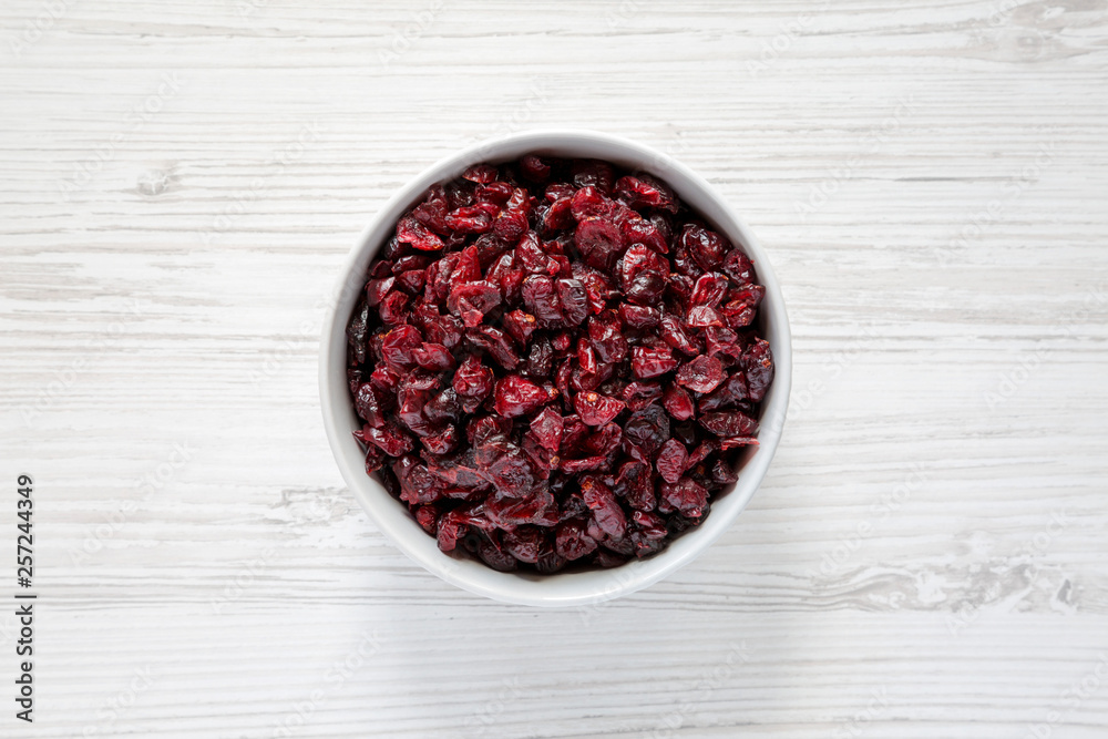 Full bowl of dry organic cranberries over white wooden surface, top view. Overhead, from above, flat lay. Close-up. Full bowl of dry organic cranberries over white wooden surface, top view. Overhead, from above, flat lay. Close-up.
